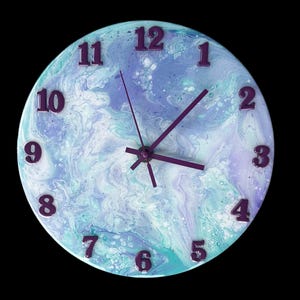 Puede incluir: Un reloj redondo con un diseño de mármol azul y blanco. La esfera del reloj tiene números y manecillas morados.