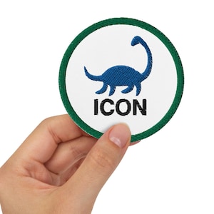 May include: A round patch with a white background, a blue dinosaur silhouette, and the word "ICON" in black. The patch has a green border and is held by a hand.