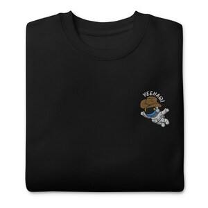 May include: Black sweatshirt with an embroidered image of a cartoon astronaut wearing a cowboy hat. The astronaut is floating in space and the text "Yeehaw!" is above the astronaut.