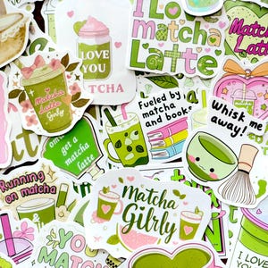 May include: A collection of colorful stickers with matcha-themed designs. The stickers feature phrases like "Matcha Girly," "I love matcha," and "Whisk me away!" in green and pink. Some stickers depict matcha lattes and cups.