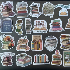 May include: A collection of colorful book-themed stickers featuring stacks of books, open books, and quotes about reading. The stickers are on a gray laptop.