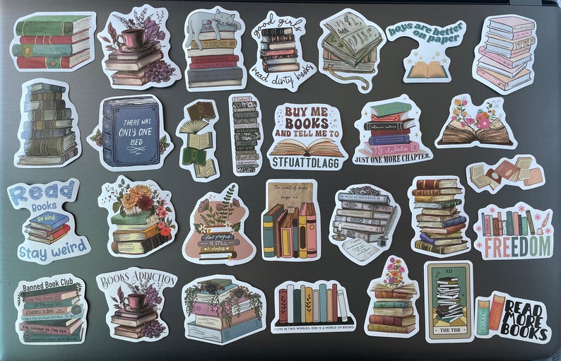 May include: A collection of colorful book-themed stickers featuring stacks of books, open books, and quotes about reading. The stickers are on a gray laptop.