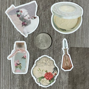 May include: A collection of vintage-style stickers featuring a statue with floral accents, a compact, a perfume bottle, a bottle with a bird illustration, and a floral design. A U.S. quarter is also present.