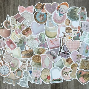 May include: A selection of pastel-coloured, vintage-style stickers. The stickers depict cherubs, hearts, bows, and other decorative elements. Some stickers include text, such as "Summer in Scotland" and "The Dreams of a Pink Christmas."