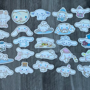 Pu&ograve; includere: Una collezione di adesivi fustellati con un personaggio dei cartoni animati con lunghe orecchie. Gli adesivi raffigurano il personaggio in varie pose e abiti, tra cui un cappello da chef, un cappello invernale e un berretto da baseball. Alcuni adesivi hanno la parola "CUTE".