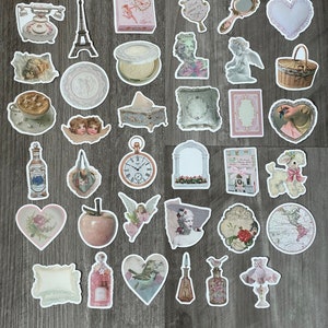 May include: A selection of vintage-style stickers with diverse designs. Includes images of an Eiffel Tower, cherubs, a pocket watch, perfume bottles, hearts, and a poodle. The stickers have a soft, pastel colour palette with floral and antique elements.
