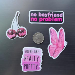 May include: A collection of stickers with a pink theme. Includes a sticker with the text "no boyfriend no problem", a butterfly, a pair of disco ball cherries, and a sticker with the text "you're like really pretty". A quarter is also included.