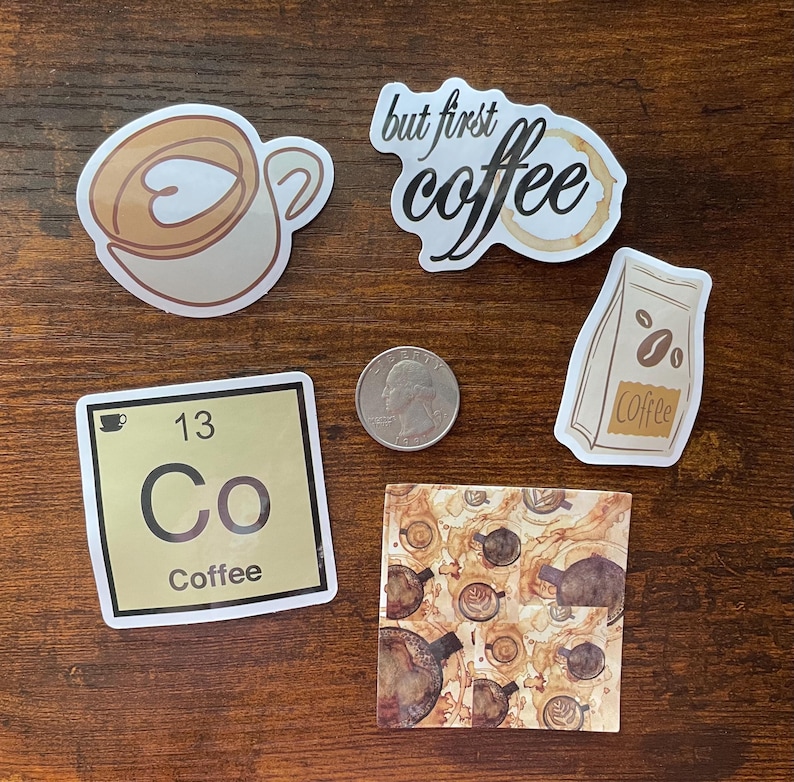 May include: A collection of five coffee-themed stickers including a latte cup, a script text sticker reading but first coffee, a coffee bean bag, a periodic table element square labeled 13 Co Coffee, and a square with coffee ring stains and a US quarter.