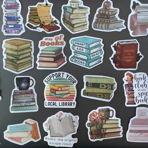 May include: A collection of 25 book-themed stickers featuring stacks of books, book-related quotes, and illustrations. The stickers are on a gray surface. Some of the quotes include "When in doubt, go to the library", "Read, books are brain food", "Way of books", "Smart kids read books", "Enemies to lovers", "A book digs every time you have a reality TV show", "My book club reads spicy books", "I like big books and I cannot lie", "Books: the original escape room".