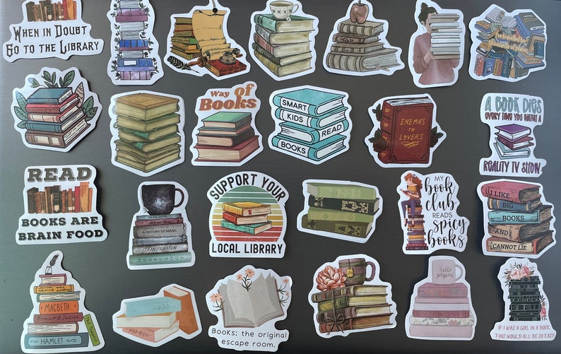 May include: A collection of 25 book-themed stickers featuring stacks of books, book-related quotes, and illustrations. The stickers are on a gray surface. Some of the quotes include "When in doubt, go to the library", "Read, books are brain food", "Way of books", "Smart kids read books", "Enemies to lovers", "A book digs every time you have a reality TV show", "My book club reads spicy books", "I like big books and I cannot lie", "Books: the original escape room".