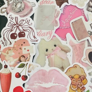 May include: A collection of pink and white stickers featuring various designs, including a vintage rotary phone, a heart with confetti, a cherub, a bunny, a pair of lips, a strawberry shortcake character, a seashell, a diary, a heart with the word "Aquarius", and a vintage lighter.