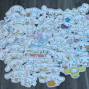 Pu&ograve; includere: Una collezione di adesivi bianchi con un personaggio dei cartoni animati con lunghe orecchie e vari accessori. Alcuni adesivi hanno il testo "CUTE". Gli adesivi sono disposti su una superficie di legno.