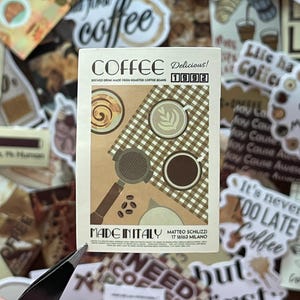 May include: A rectangular sticker featuring a tan and brown graphic of coffee items. Text reads COFFEE, Delicious! 1992, BREWED DRINK MADE FROM ROASTED COFFEE BEANS, MADE IN ITALY, and MATTEO SCHILIZZI 17 16163 MILANO. It shows a portafilter, coffee beans, and cups.