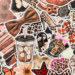 May include: A collection of stickers featuring various designs, including a brown teddy bear, a brown bow, a leopard print shoe, a leopard print bow, a leopard print heart, a leopard print star, a leopard print pattern, a cup of iced coffee, a stack of books, a butterfly, a flower, and a leopard print animal.