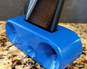 May include: A blue 3D printed phone stand with two circular cutouts on the front. A black smartphone is placed in the stand.