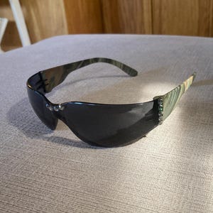 May include: Camouflage print sunglasses with black lenses and rhinestones on the arms.