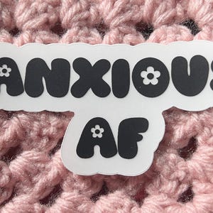 May include: A white sticker with black text that reads "ANXIOUS AF" in a bubble font. The letters have small white flowers on them.