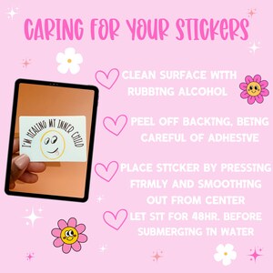 May include: Pink background with instructions on how to care for stickers. The instructions include cleaning the surface with rubbing alcohol, peeling off the backing, pressing the sticker firmly, and letting it sit for 48 hours before submerging in water. The image also includes a cartoon flower and a sticker that says "I'm healing my inner child."