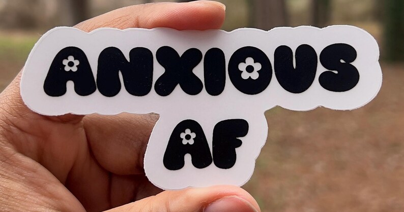 May include: White sticker with black text that reads "ANXIOUS AF" with a small white flower in each letter.