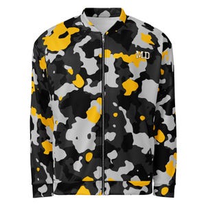 Peut inclure: Un blouson zippé avec un motif camouflage noir, gris et jaune. Le vêtement présente un col montant, des manches longues et les lettres MD imprimées en blanc sur la poitrine gauche. L'avant est doté d'une fermeture éclair intégrale.