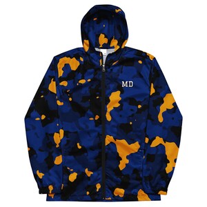 May include: A hooded windbreaker jacket featuring a camouflage pattern in shades of blue, black, and yellow. The jacket has a full-length black front zipper and the letters MD printed in a light yellow font on the upper right chest area.