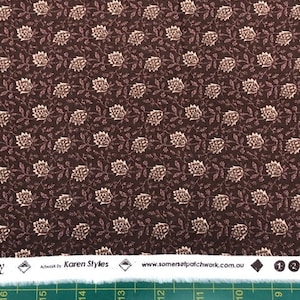 Könnte beinhalten: Brauner Stoff mit einem sich wiederholenden Muster aus kleinen, hellbraunen Blumenmotiven. Der Stoff hat einen weißen Rand mit dem Text "Artwork by Karen Styles" und "www.somersetpatchwork.com.au".