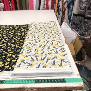 Könnte beinhalten: Zwei Stoffstücke mit einem Blumenmuster. Ein Stoff ist weiß mit gelben Blumen und grünen Blättern. Der andere Stoff ist schwarz mit gelben Blumen und grünen Blättern.