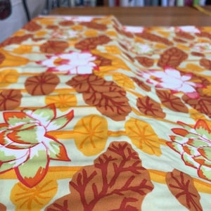 Könnte beinhalten: Ein weißer Stoff mit einem sich wiederholenden Muster aus orangefarbenen, roten und grünen stilisierten Blättern und Blüten. Der Stoff hat eine subtile Textur.
