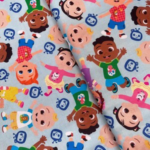 Op de afbeelding: Een blauwe stof met een herhalend patroon van cartoonfiguren. De figuren zijn allemaal baby's met verschillende huidtinten en haarkleuren. Ze dragen kleurrijke kleding en houden speelgoed vast. Er zijn ook kleine blauwe en witte televisieschermen in het patroon.