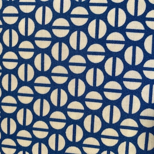 May include: Close-up of a blue and white fabric with a repeating pattern. The pattern consists of white circles with a white horizontal line and a vertical line through the centre, set against a blue background.