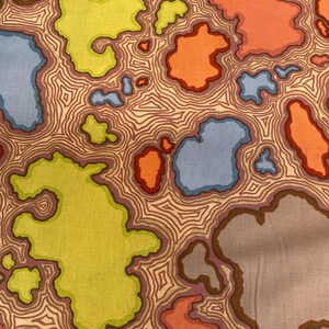 May include: A patterned fabric with an abstract design. The fabric displays irregular shapes in yellow, orange, blue, and grey, outlined in brown, set against a beige background with brown contour lines. The fabric has a unique, artistic appearance.