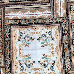 Puede incluir: Una tela blanca con un diseño estampado en negro, marrón y dorado. El patrón presenta un motivo floral repetitivo con detalles intrincados.