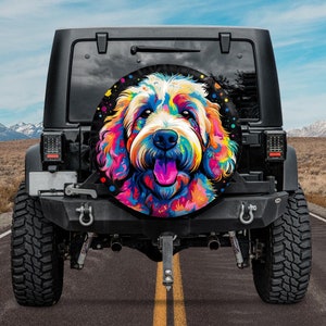 Puede incluir: Un Jeep negro con una ilustración colorida de un perro en la cubierta de la rueda de repuesto. El perro es un doodle con la lengua rosa y una expresión feliz. La cubierta de la rueda es un círculo negro redondo con puntos blancos.