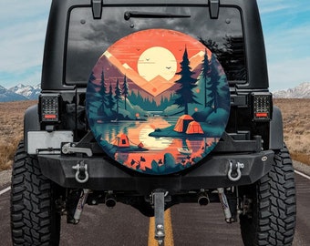 Pode incluir: Um Jeep preto com uma capa de pneu sobressalente com uma ilustração de acampamento. A obra de arte retrata uma cena de lago com tendas laranja, montanhas, árvores e um pôr do sol. O Jeep está estacionado em uma estrada pavimentada.