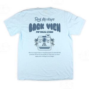 May include: Pale blue t-shirt featuring a retro camera graphic and palm trees. The text on the shirt reads "Real Mockups BACK VIEW POP MOCKS STUDIO". Further text is printed below the graphic.