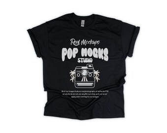 May include: A black short-sleeve t-shirt featuring white text that reads Real Mockups POP MOCKS STUDIO above a graphic of a camera with palm trees. Smaller text below the camera reads All of our images feature real photographs of authentic POD products.