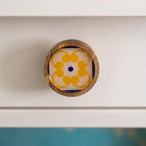 May include: A round wooden knob with a yellow and blue floral design. The knob is perfect for adding a touch of color and style to any cabinet or drawer.