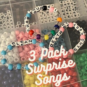 Pu&ograve; includere: Tre braccialetti colorati con perline con le parole "Clean", "Death By 1000 Cuts" e "Eras Tour" scritte. I braccialetti sono in un contenitore di plastica con altre perline.