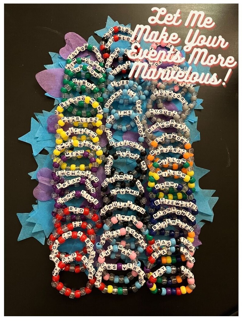 Pu&ograve; includere: Una collezione di braccialetti colorati con perline, con parole come "Taylor Swift", "1989", "Delicate", "Reputation", "Cruel Summer" e "Lover" scritte su di essi. I braccialetti sono disposti in cerchio su uno sfondo blu con stelle.