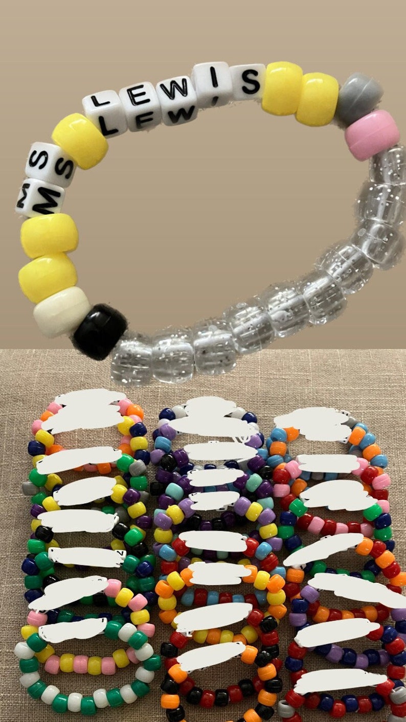 Pu&ograve; includere: Una collezione di braccialetti colorati con perline, tra cui un braccialetto con il nome "MS LEWIS" scritto in lettere bianche su perline nere.
