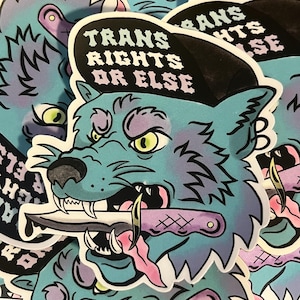 May include: A sticker featuring a teal wolf with a black hat that reads "TRANS RIGHTS OR ELSE". The wolf has a knife in its mouth and is set against a blue background. The sticker has a cartoon style.