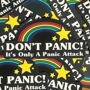 May include: A black and white sticker with a rainbow arc and stars. The sticker reads "Don't Panic! It's Only A Panic Attack".