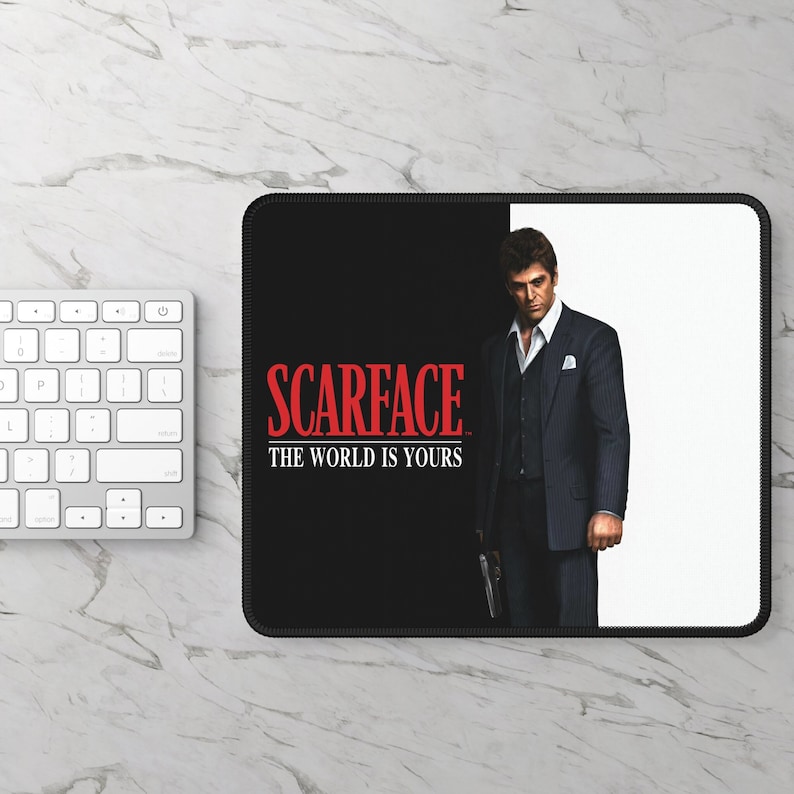 May include: Black and white mousepad with a red "Scarface" logo and the text "The World Is Yours". A man in a suit is standing on the right side of the mousepad.