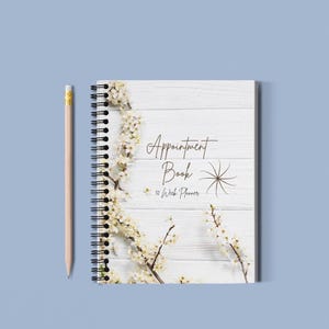 May include: A white appointment book with a floral design and the text "Appointment Book 52 Week Planner" on a white wood background.