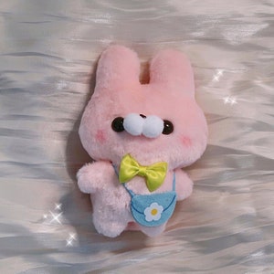 May include: A pink plush bunny with a yellow bow tie and a light blue bag with a white flower on it.