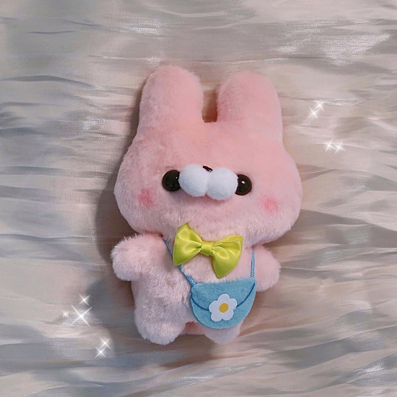 May include: A pink plush bunny with a yellow bow tie and a light blue bag with a white flower on it.