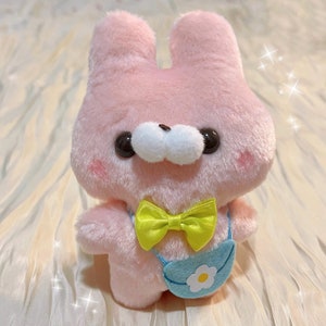 May include: A pink plush bunny with a yellow bow tie and a blue and white bag with a flower design.