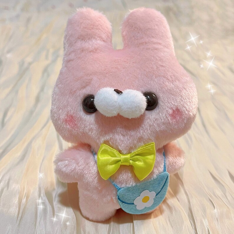 May include: A pink plush bunny with a yellow bow tie and a blue and white bag with a flower design.