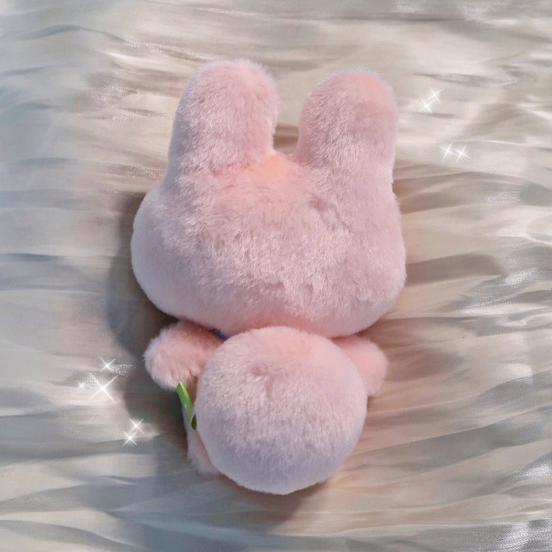 May include: A pink plush bunny toy with a fluffy tail. The bunny is sitting on a white surface.