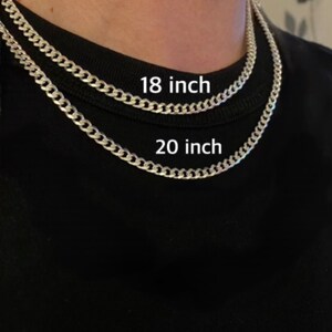 May include: Two silver chain necklaces, one 18 inches long and the other 20 inches long, are shown on a person's neck. The necklaces are both curb chain style.
